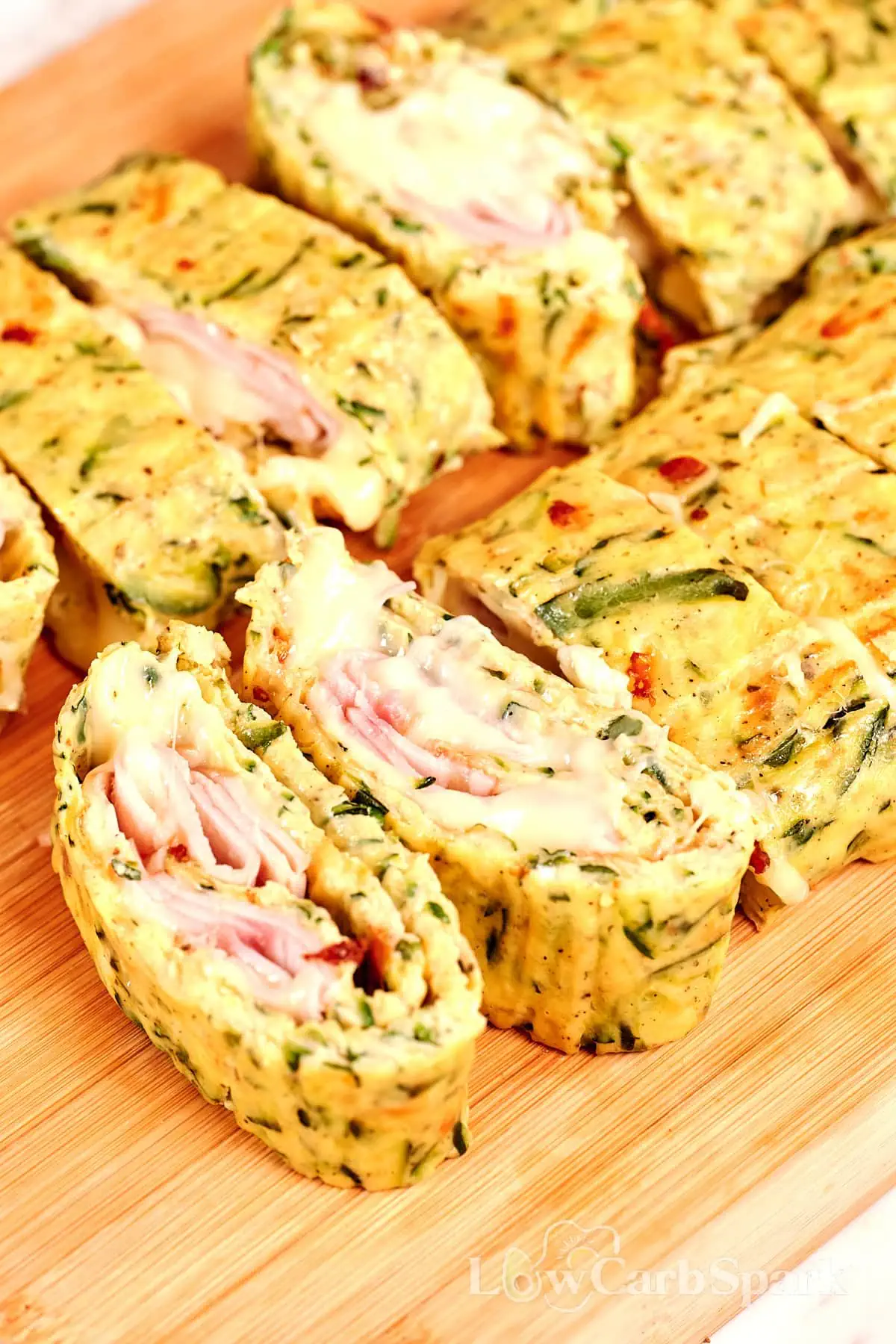 Zucchini Ham and Cheese Roll 3 Sliced zucchini ham and cheese roll on a wooden board with melted cheese filling.