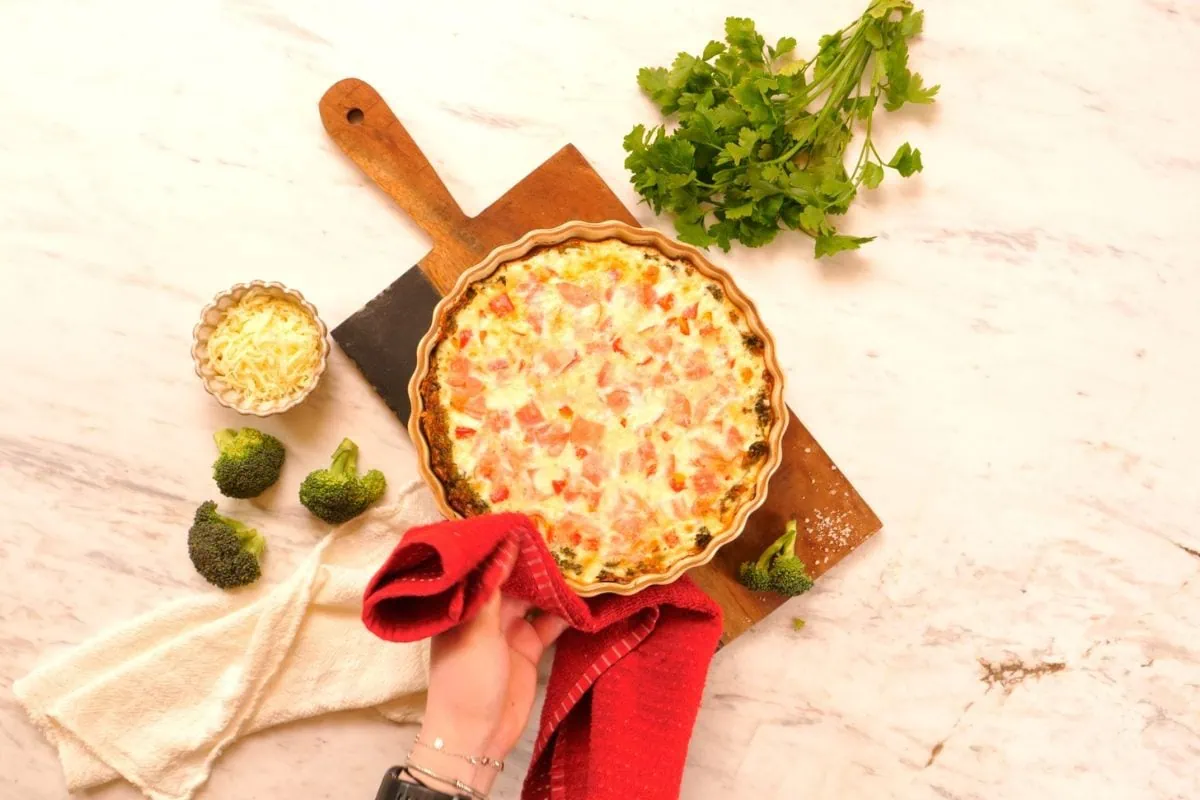 Cheesy Broccoli Crust Quiche 8 Freshly baked cheesy broccoli crust quiche served in a tart pan on a wooden board.