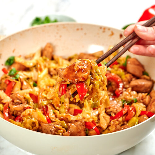 Chicken and Cabbage Stir Fry 14 Chopsticks lifting chicken, cabbage, and red bell peppers coated in savory stir-fry sauce from a skillet.