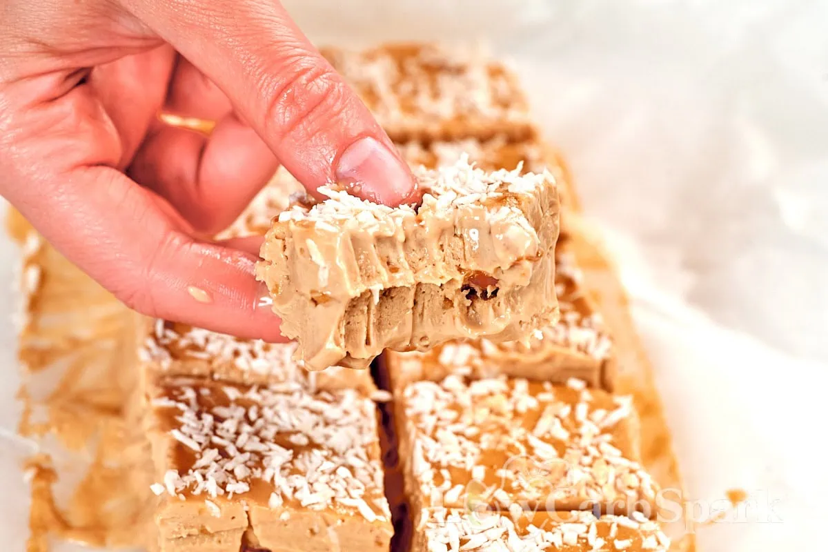 No-Bake Peanut Butter Greek Yogurt Protein Bars 2 Hand holding a no-bake peanut butter Greek yogurt protein bar topped with coconut flakes, highlighting the soft and creamy center.