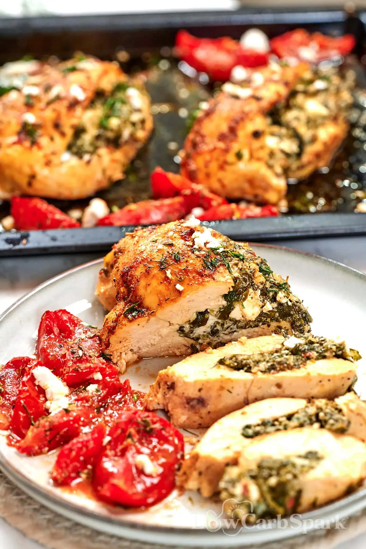 Spinach and Feta Stuffed Chicken Breast 2 Sliced spinach and feta stuffed chicken breast served with roasted tomatoes, showing the creamy feta and spinach filling inside the juicy chicken.