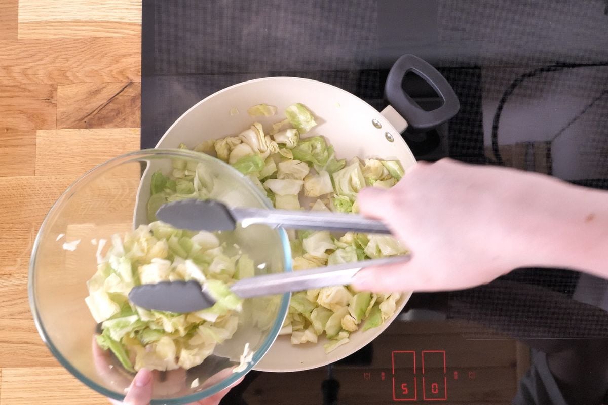 One-Pan Cajun Beef and Cabbage Skillet 7 Removing sautéed cabbage from a skillet and transferring it to a bowl.
