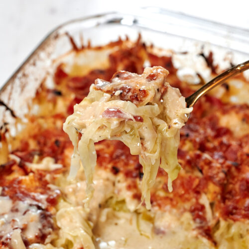 Chicken Alfredo Cabbage Bake 10 Fork lifting a cheesy bite of Chicken Alfredo Cabbage Bake with tender chicken, cabbage noodles, crispy bacon, and creamy Alfredo sauce.