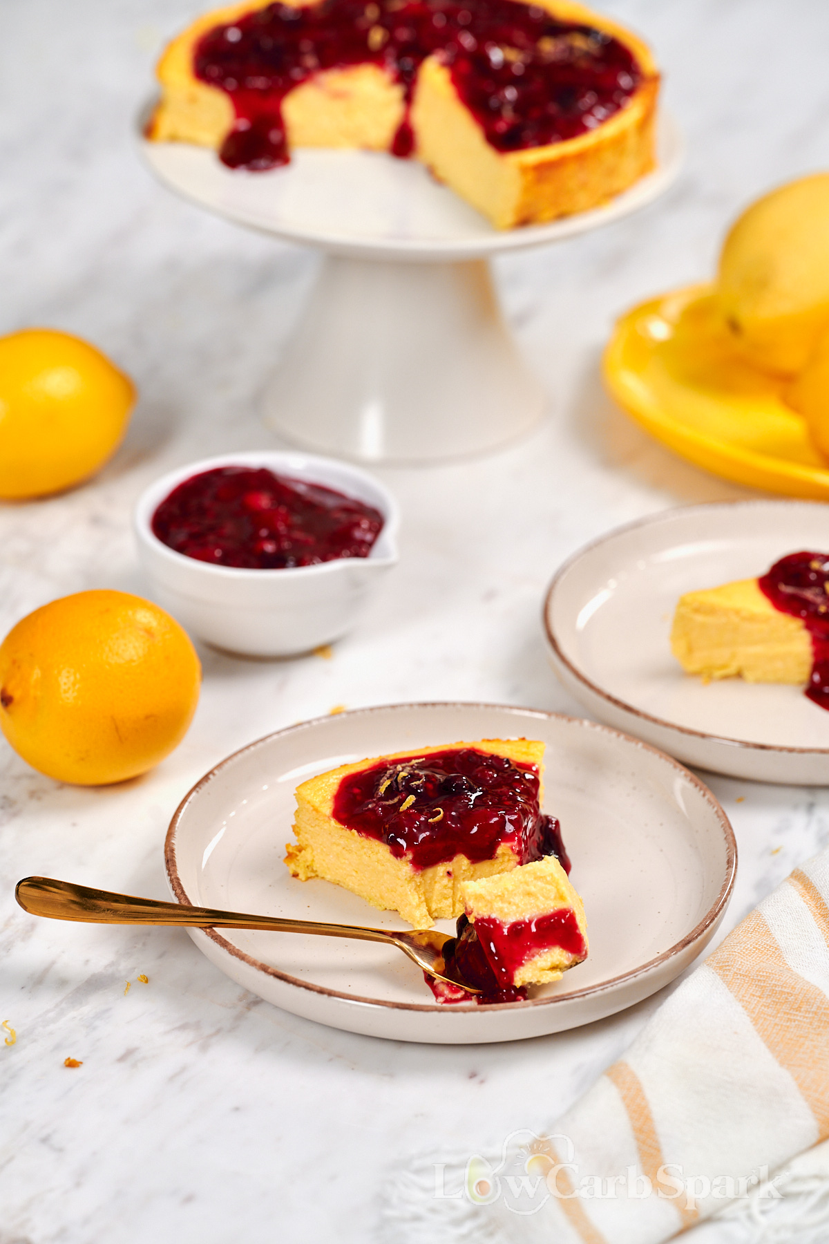 Cottage Cheese Lemon Cheesecake 2 Slice of cottage cheese lemon cheesecake topped with homemade berry sauce, served on a dessert plate with fresh lemons in the background.