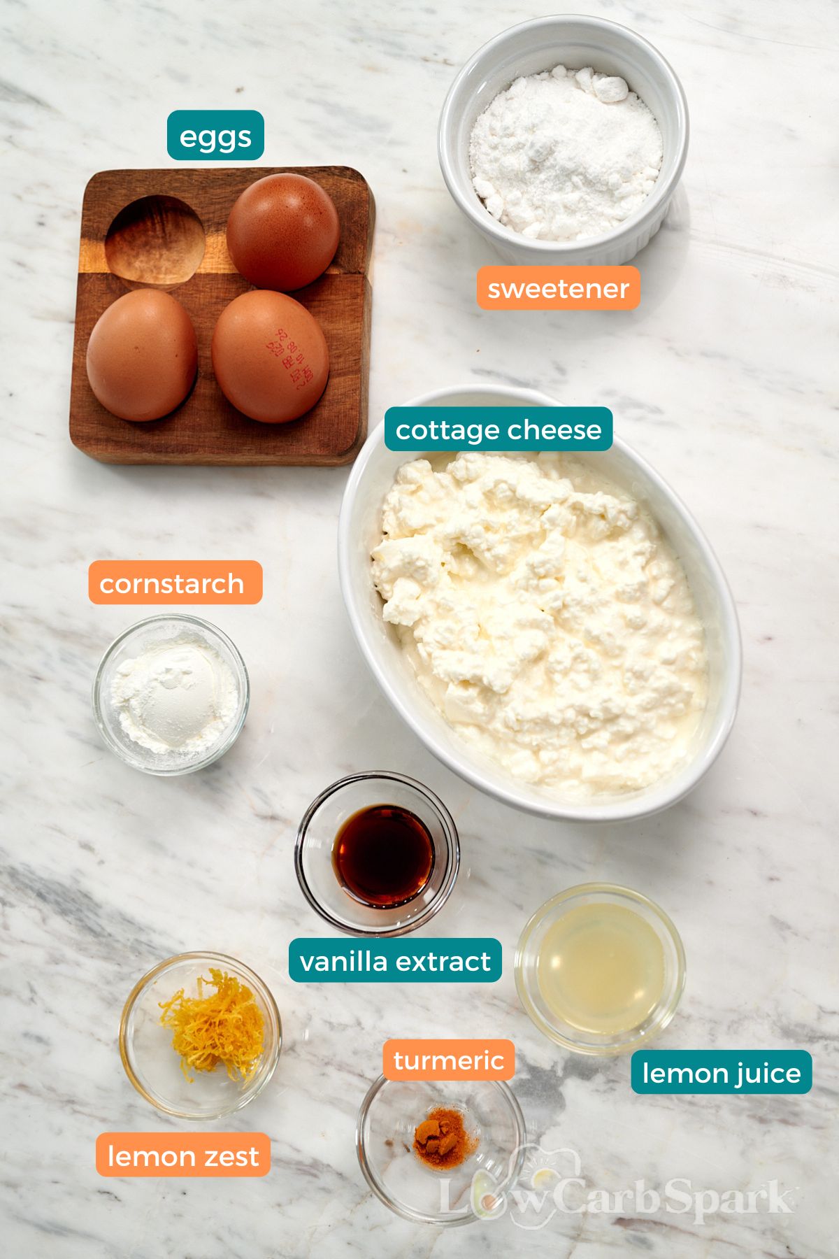 Cottage Cheese Lemon Cheesecake 3 Ingredients for cottage cheese lemon cheesecake arranged on a marble countertop, including cottage cheese, eggs, powdered sweetener, vanilla, lemon juice, lemon zest, cornstarch, and turmeric.