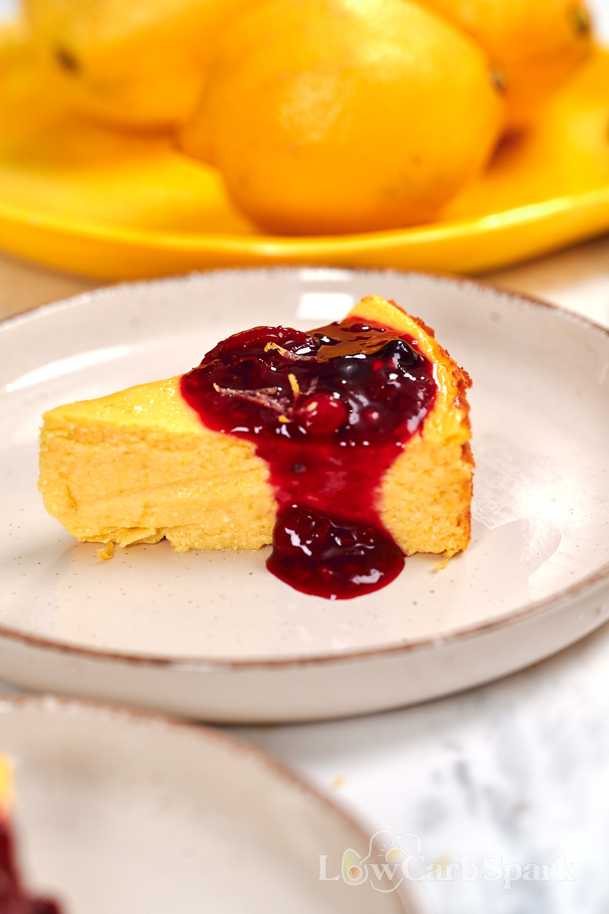 Cottage Cheese Lemon Cheesecake 12 Creamy slice of cottage cheese lemon cheesecake with a rich berry topping and fresh lemon zest served on a white plate.