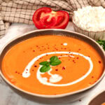 Creamy high-protein tomato soup made with roasted tomatoes and cottage cheese, topped with a swirl of cream, fresh basil, and red pepper flakes.