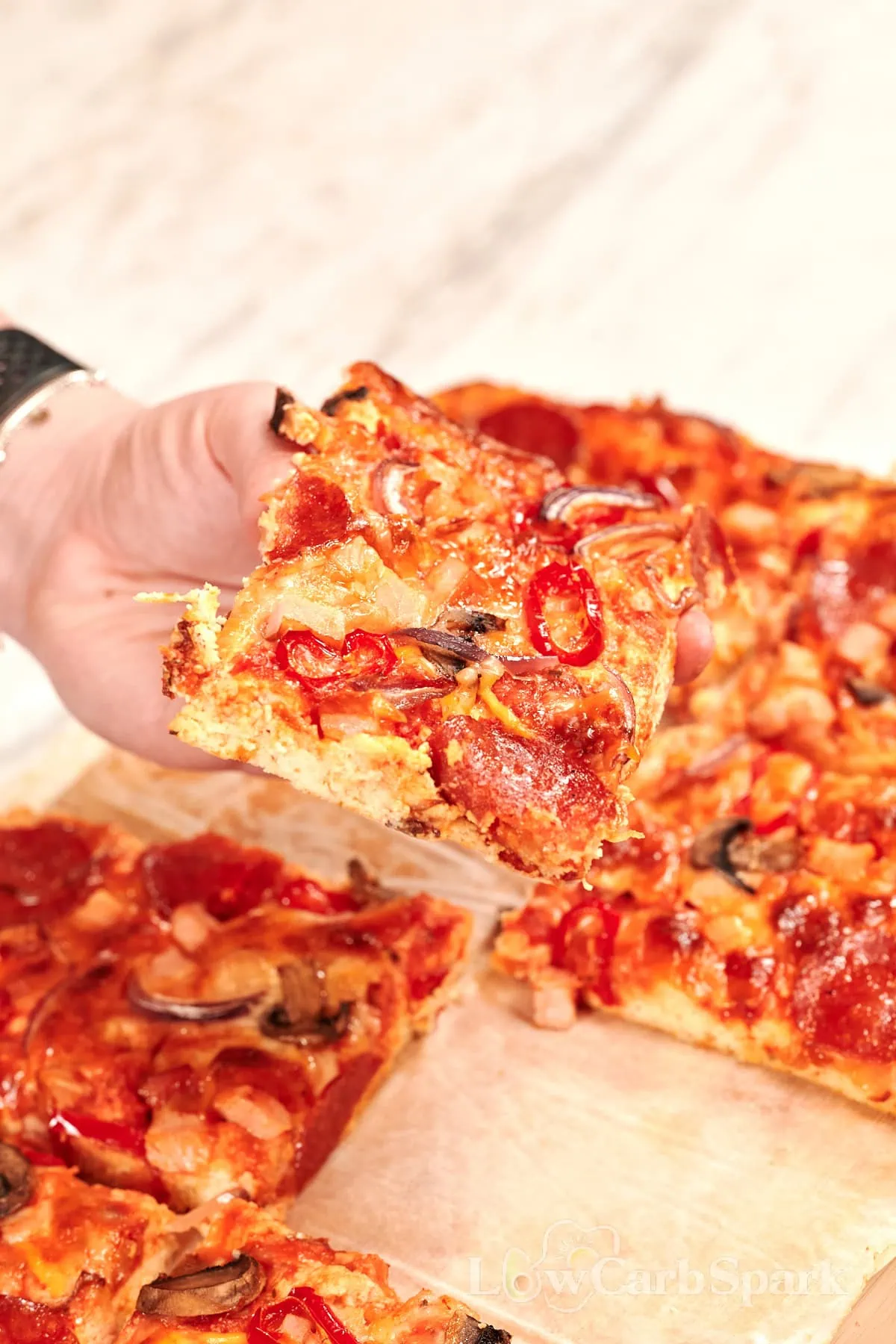Sheet Pan Cottage Cheese Pizza 1 Hand holding a slice of sheet pan cottage cheese pizza with pepperoni, mushrooms, red onion, and melted cheese on a thick high-protein crust.