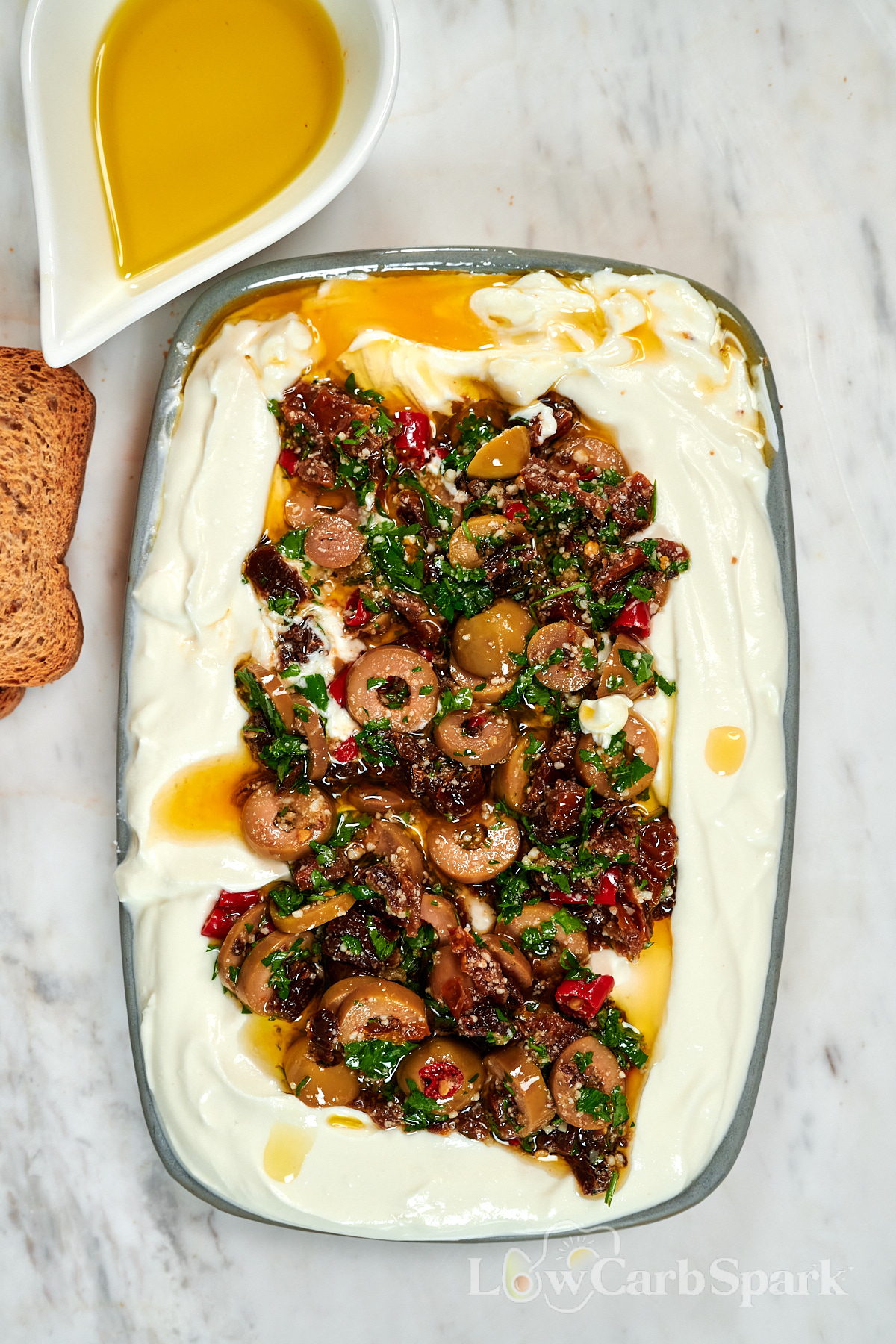 Whipped Cottage Cheese Dip with Sun-Dried Tomatoes 3 Overhead view of whipped cottage cheese dip topped with chopped sun-dried tomatoes, green olives, garlic, parsley, Parmesan, and extra virgin olive oil.