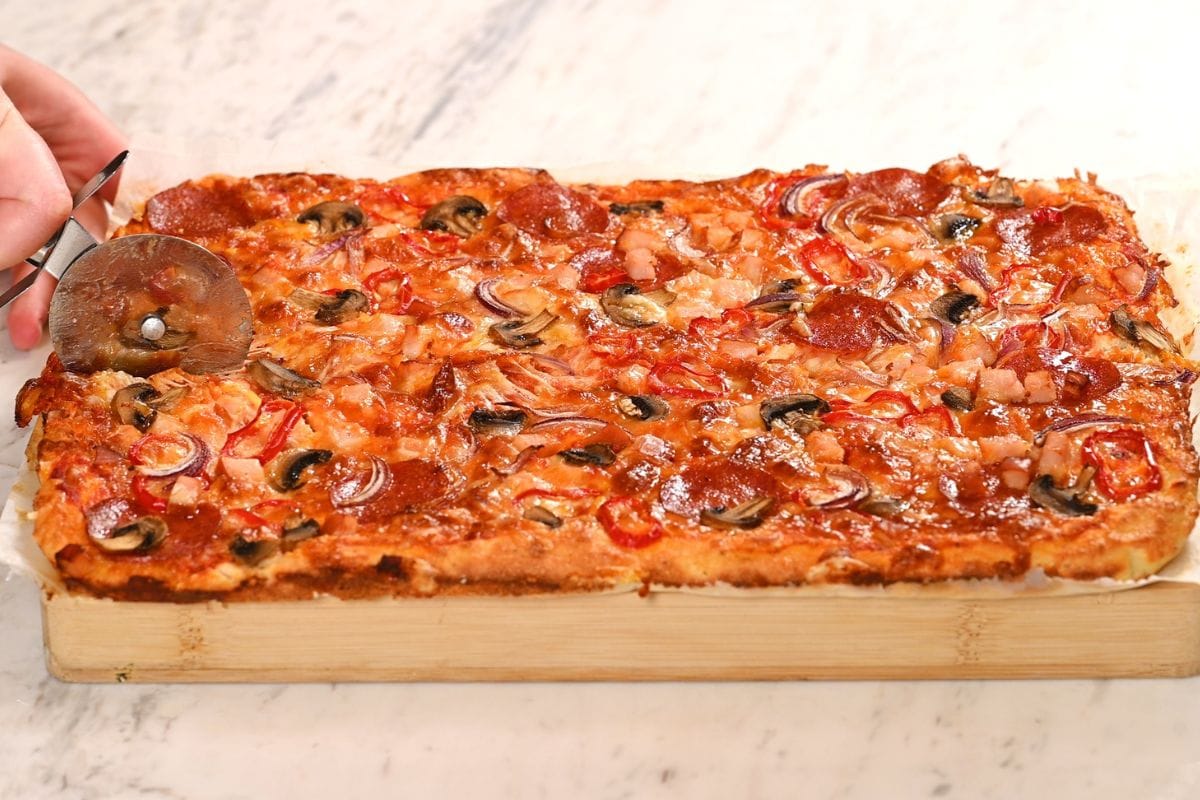 Sheet Pan Cottage Cheese Pizza 6 Freshly baked sheet pan cottage cheese pizza being sliced with a pizza cutter after baking until golden and crispy.