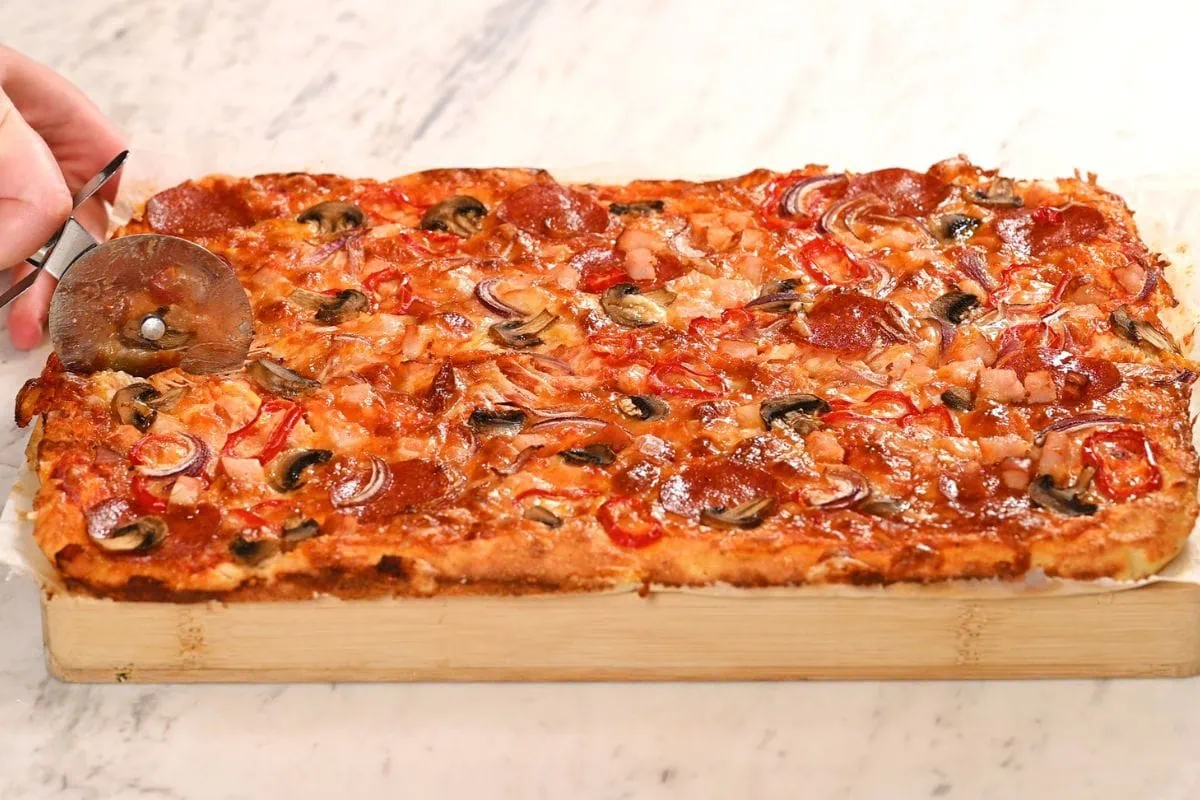 Sheet Pan Cottage Cheese Pizza 6 Freshly baked sheet pan cottage cheese pizza being sliced with a pizza cutter after baking until golden and crispy.
