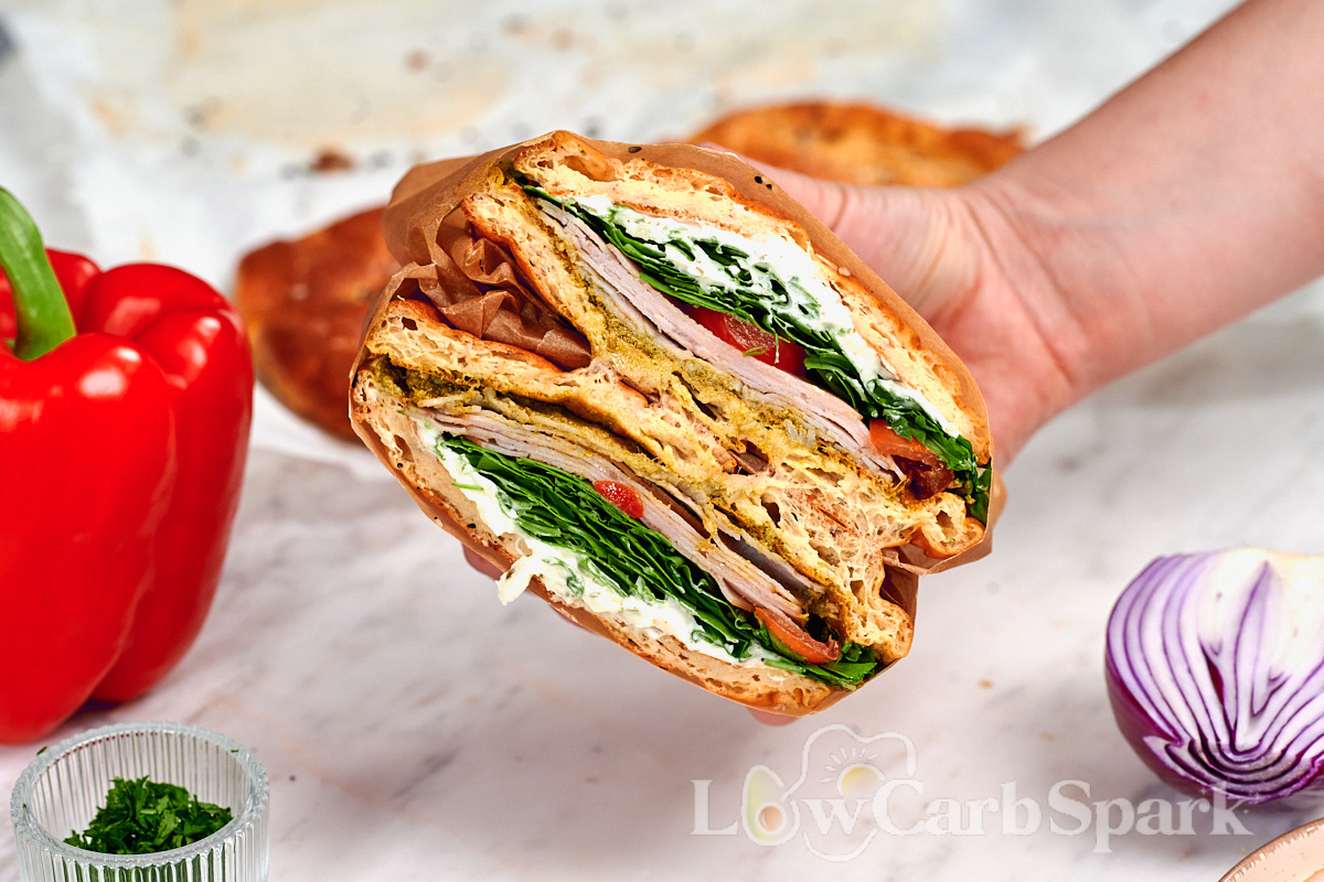 Cottage Cheese Psyllium Buns 14 Hand holding a cottage cheese psyllium bun sandwich filled with turkey, arugula, tomato, and creamy spread.