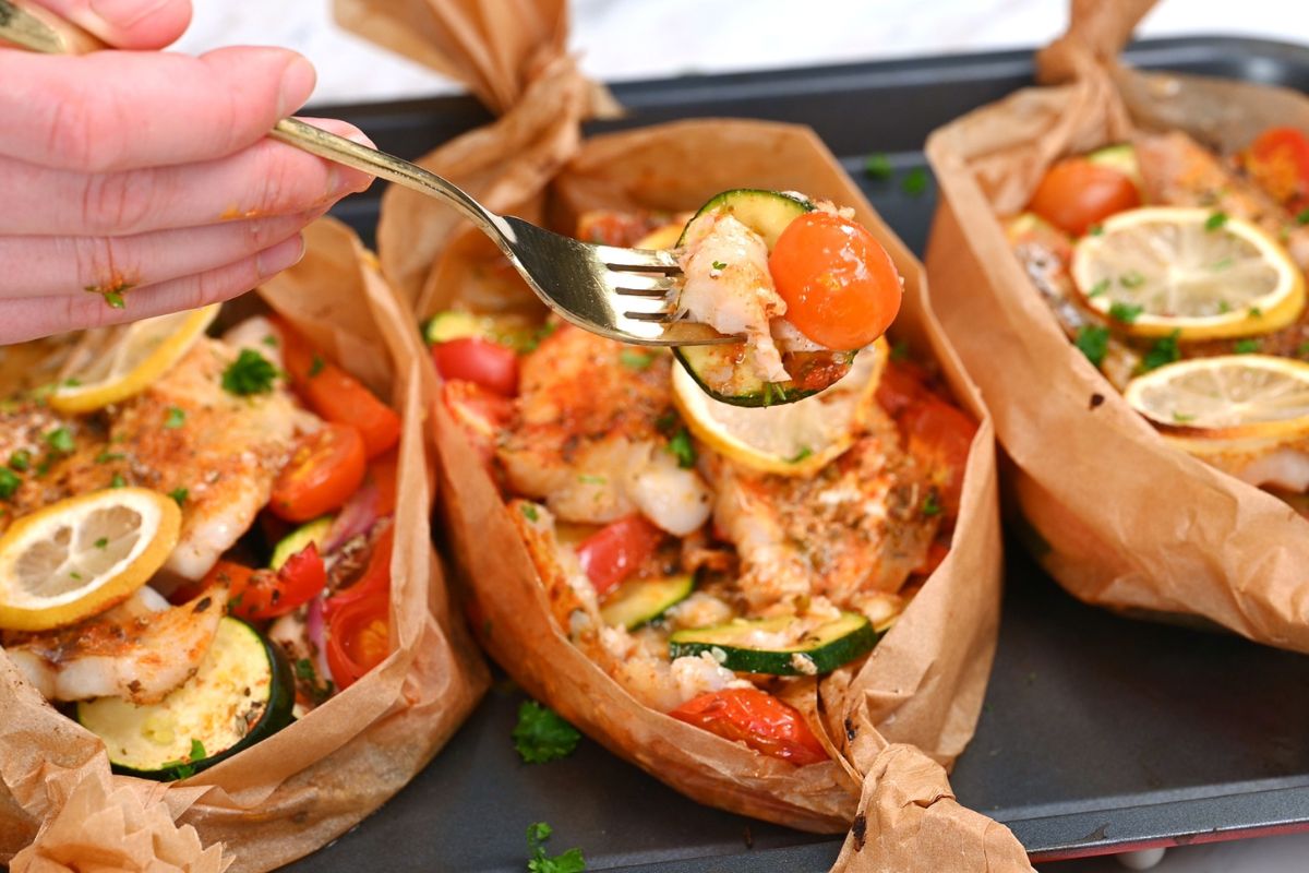 Mediterranean Baked Fish Boats 9 Fork holding a bite of Mediterranean baked fish with zucchini and cherry tomato from a parchment boat.