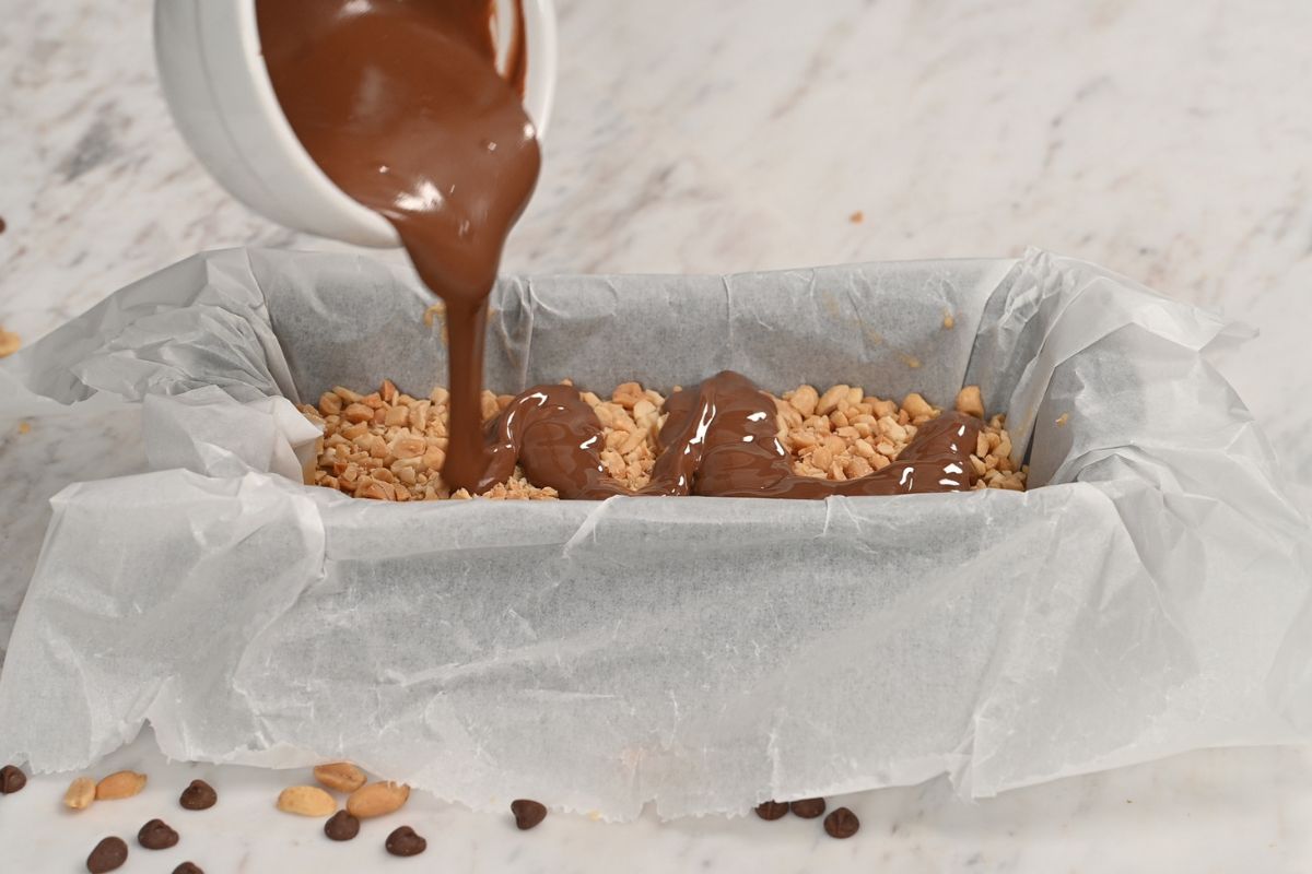 Cottage Cheese Snickers Bars 12 Pouring melted chocolate over the chopped peanut layer of high protein cottage cheese Snickers bars.