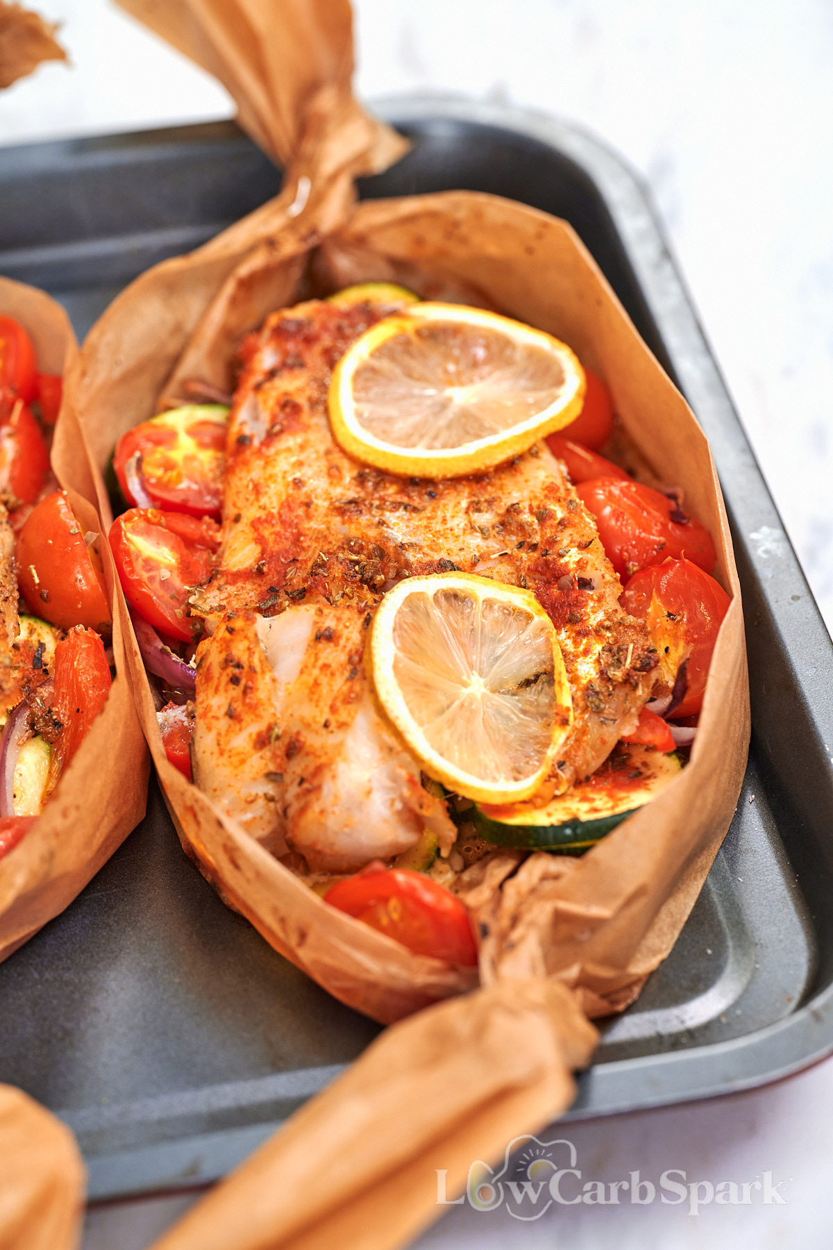 Mediterranean baked fish boat with seasoned white fish, zucchini, cherry tomatoes, red onion, and lemon slices.

