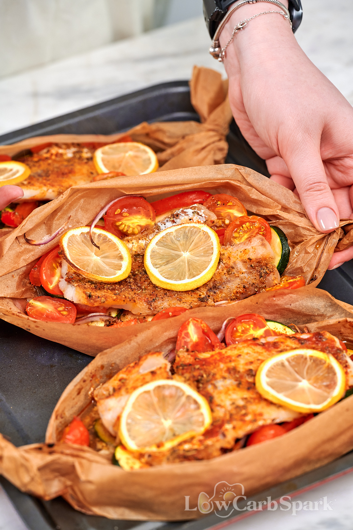 Mediterranean Baked Fish Boats 11 Hand holding a parchment baked Mediterranean fish boat filled with white fish, zucchini, tomatoes, red onion, and lemon.
