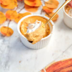 Pumpkin protein cheesecake topped with whipped cream, with a spoonful showing the creamy filling.
