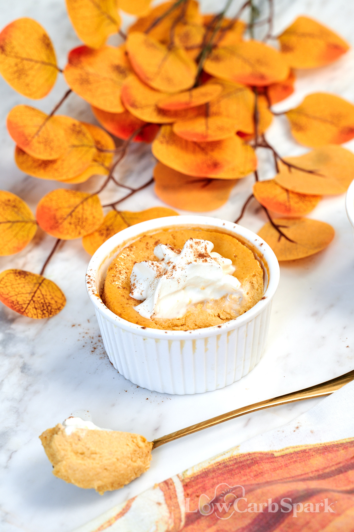Pumpkin Protein Cheesecake for Two 10 Pumpkin Spice Protein Cheesecake in a white ramekin topped with whipped cream and pumpkin spice, served with a spoonful on the side.