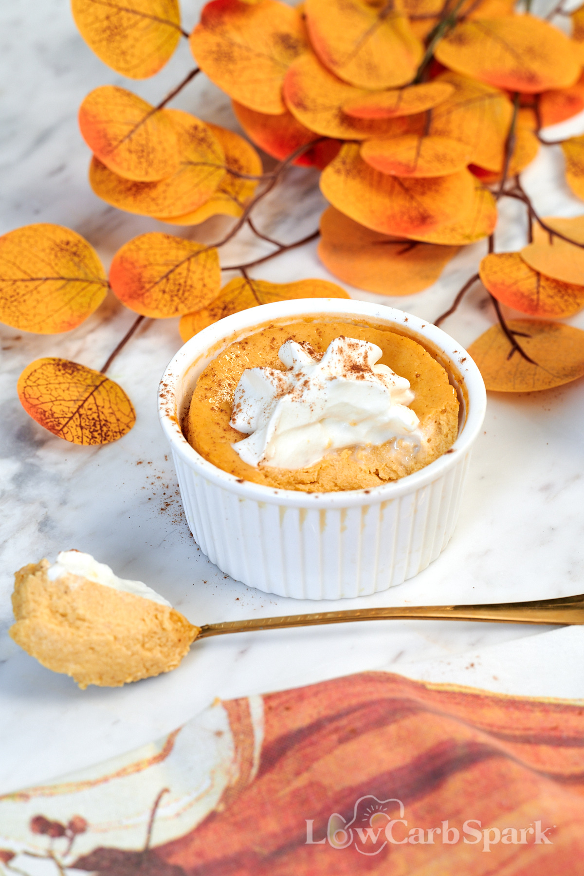 Pumpkin Protein Cheesecake for Two 2 Close-up of creamy Pumpkin Protein Cheesecake topped with whipped cream and cinnamon in a white ramekin.